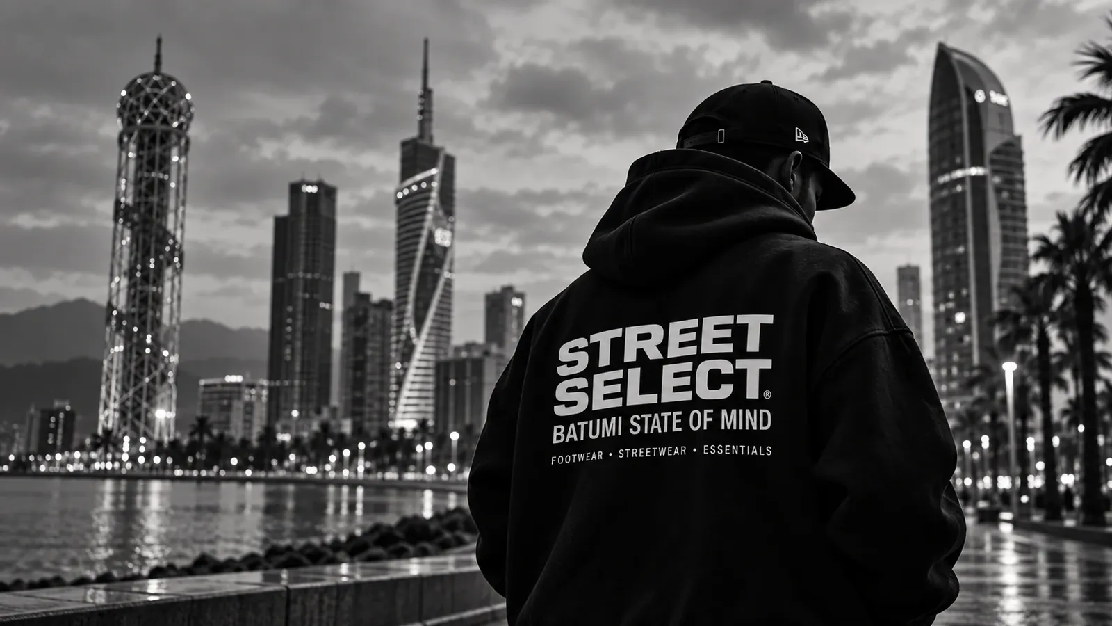 Person in a black STREET SELECT hoodie on the Batumi seafront at dusk